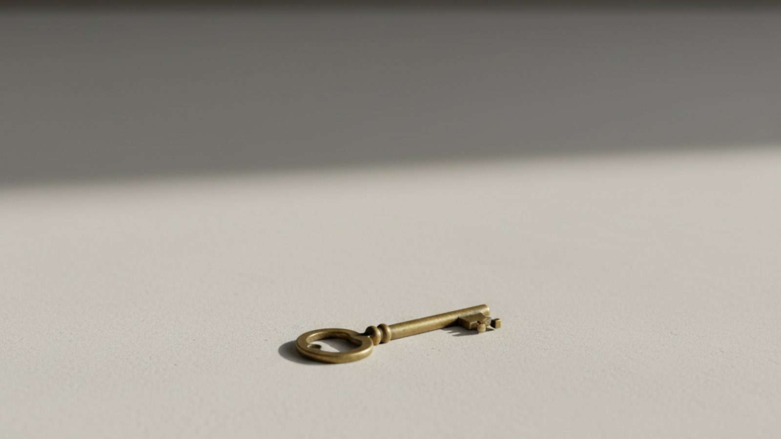 A solitary key rests on a smooth, empty surface, illuminated by gentle, directional light.